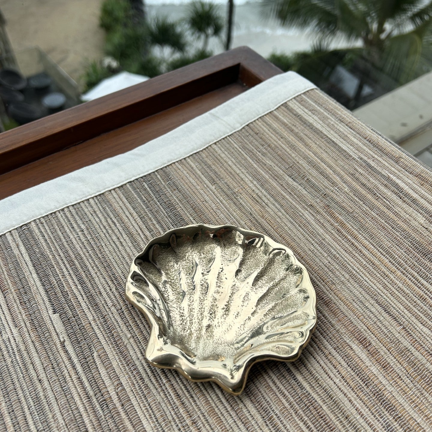 Brass shell-shaped dish on a textured surface with a blurred beach background