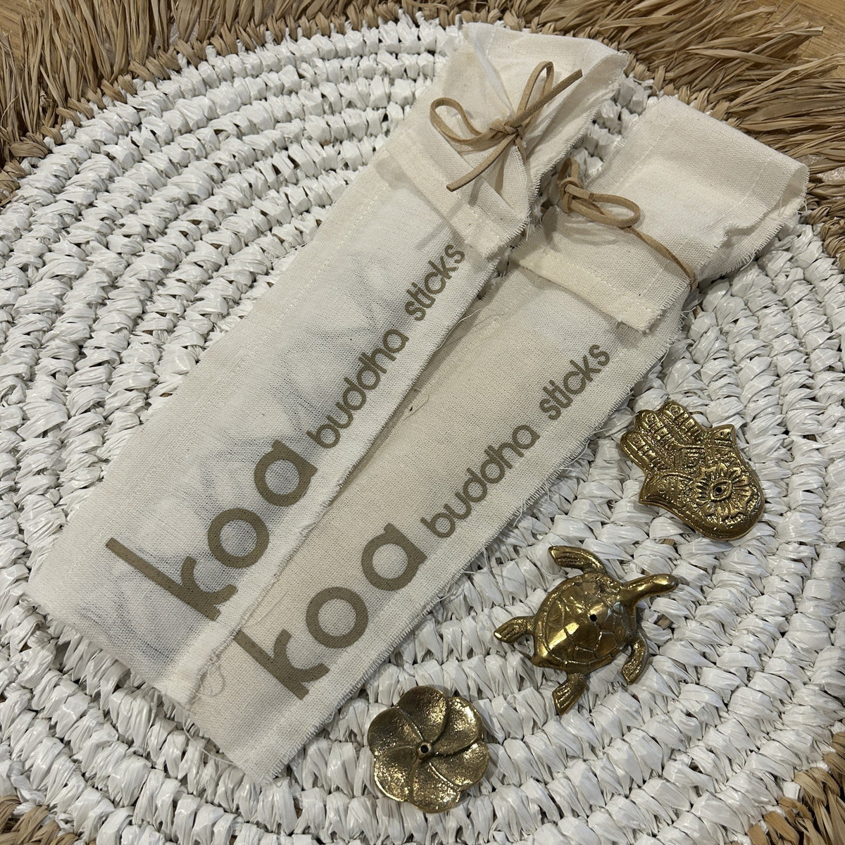 A pack of white incense sticks labeled 'Koa' placed on a woven mat, accompanied by decorative turtle and fish ornaments.