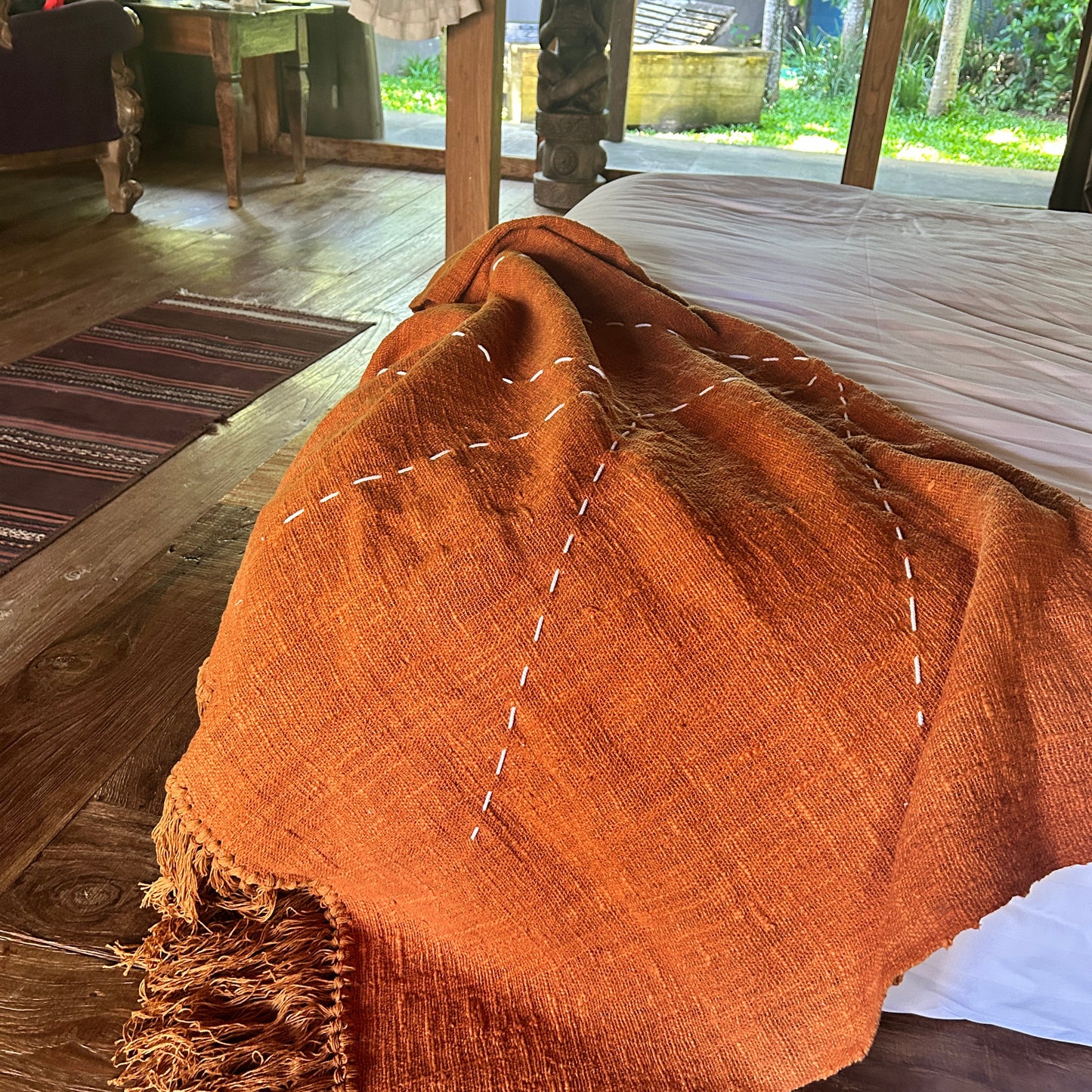 Terracotta cotton throw blanket with white stitching draped over a wooden surface