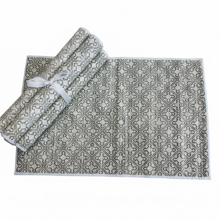 A rectangular woven textile with a repeating geometric pattern in white and natural, shown partially folded with a rolled corner and a white ribbon tie on a plain white background.