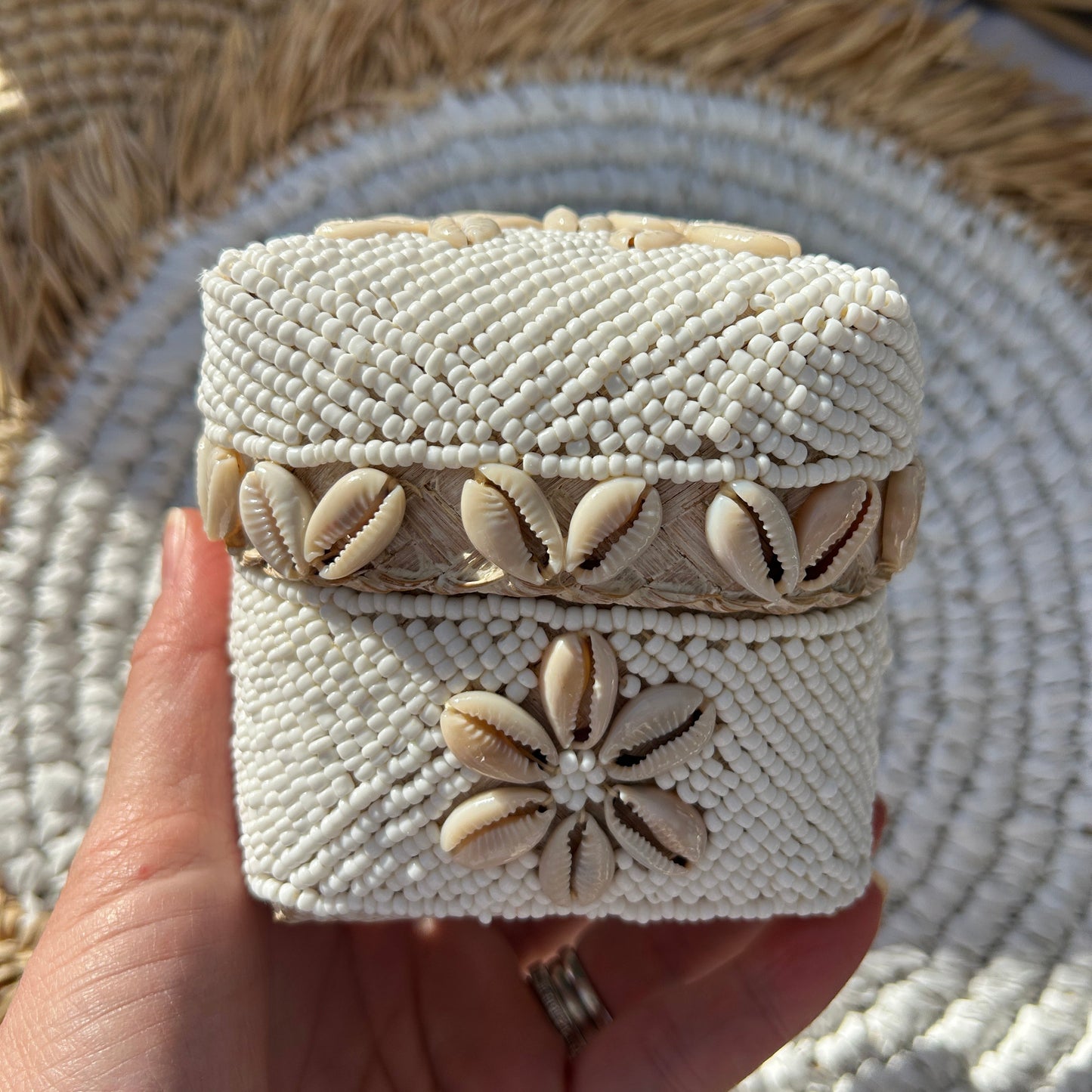 Hand holding a white hand beaded trinket box with natural coloured cowrie shell design