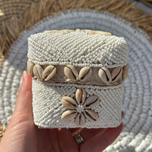 Hand holding a white hand beaded trinket box with natural coloured cowrie shell design