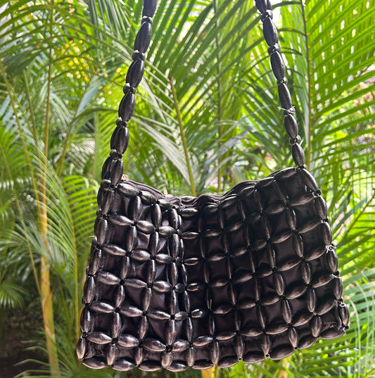 Black woven wooden bead handbag against a green leafy background