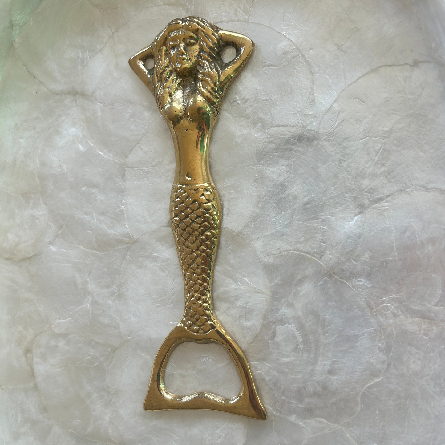 Brass bottle opener with mermaid design on a marble surface
