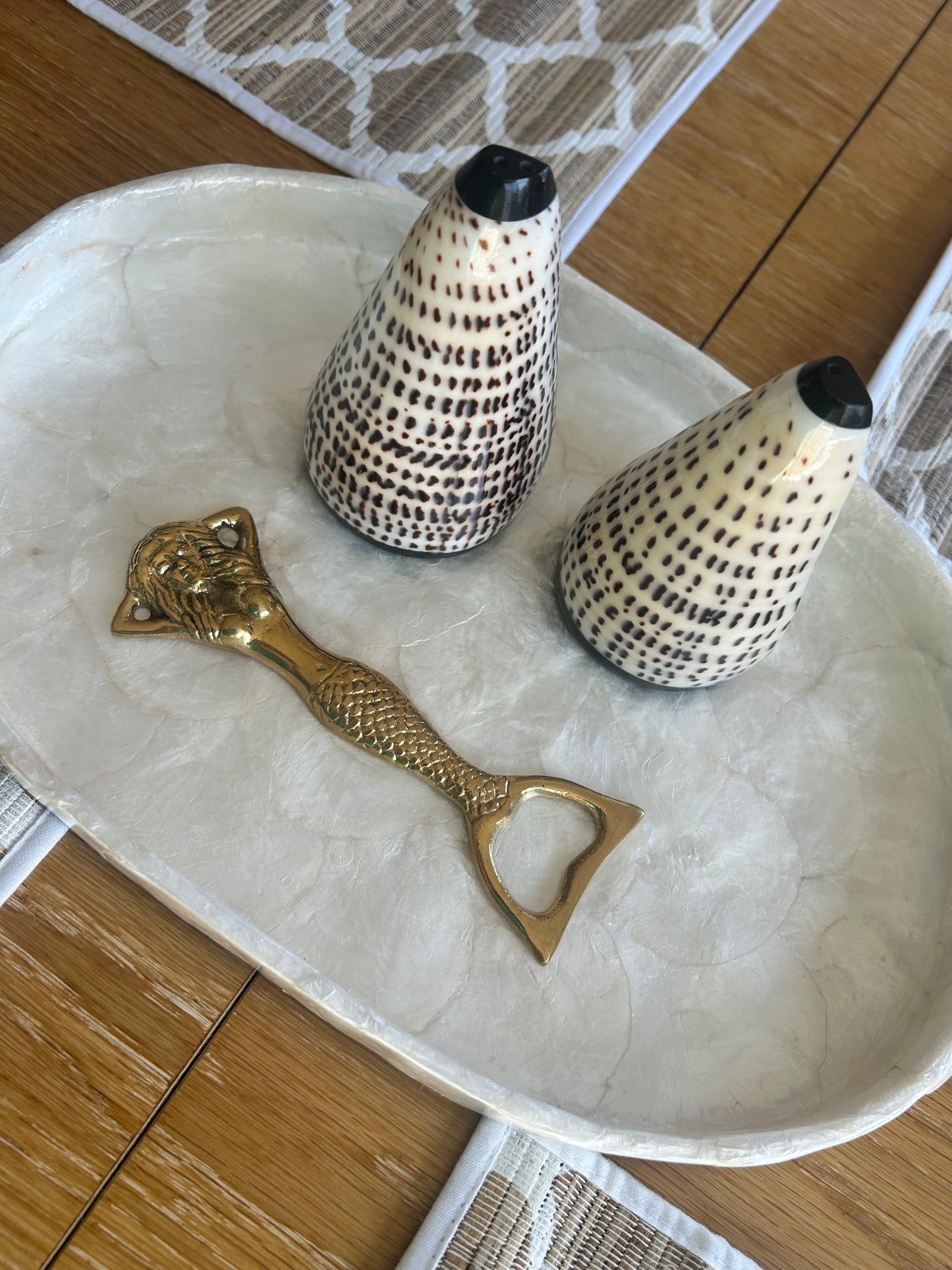 Decorative shell vases and a brass mermaid bottle opener on a marble tray.