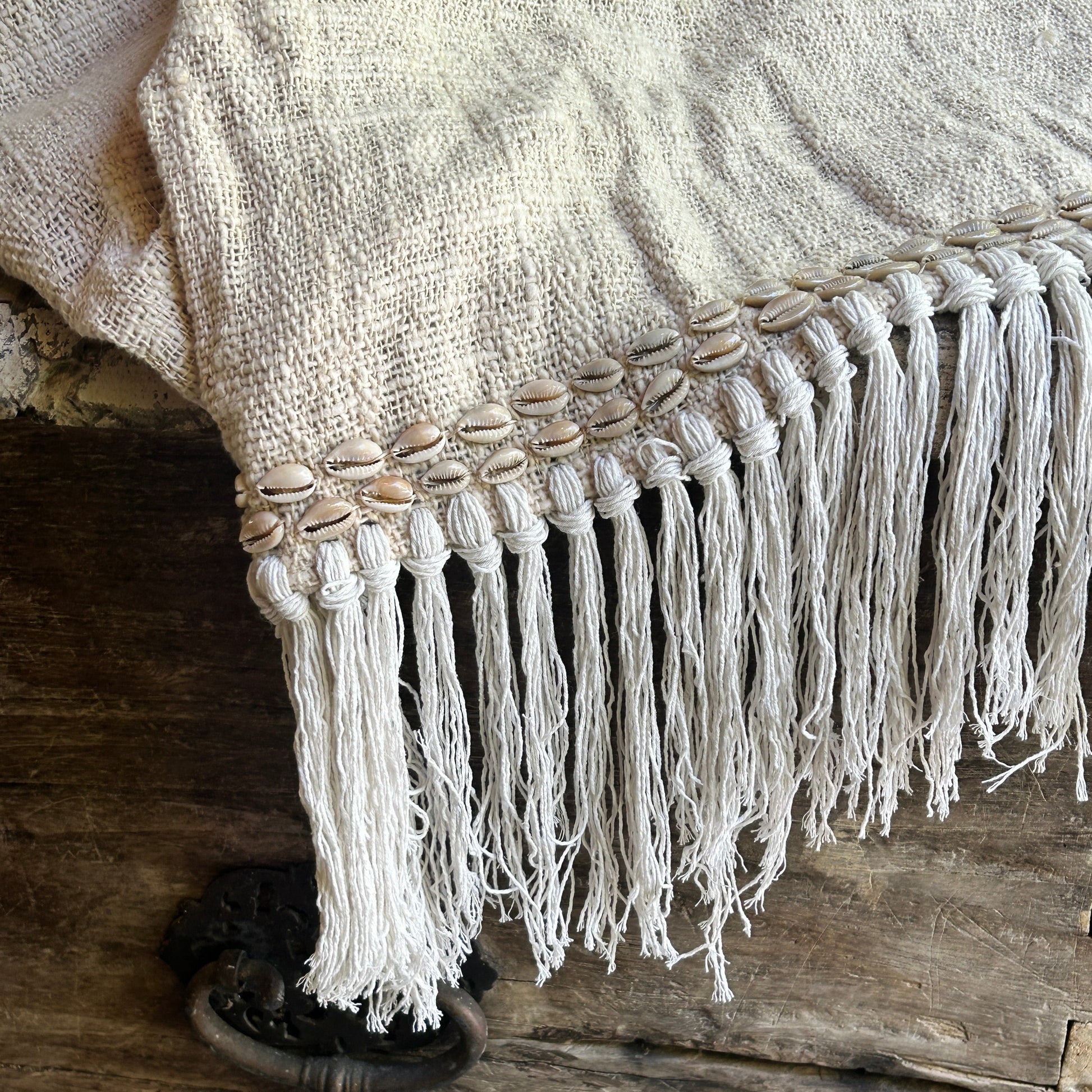 Cotton throw or blacket with fringes and shell embellishments on a wooden surface