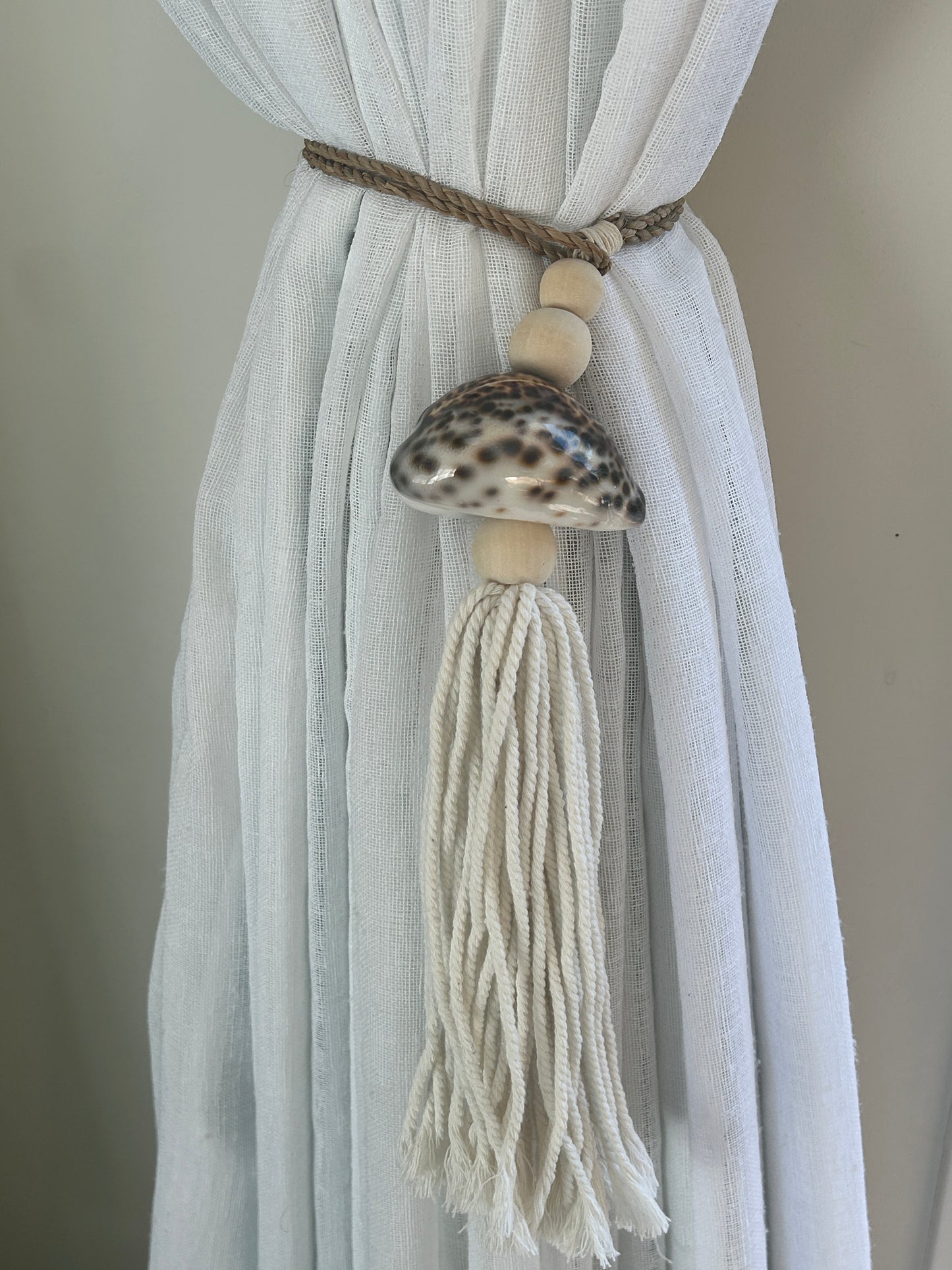 Decorative curtain tieback with shell and tassel on a white curtain against a neutral background