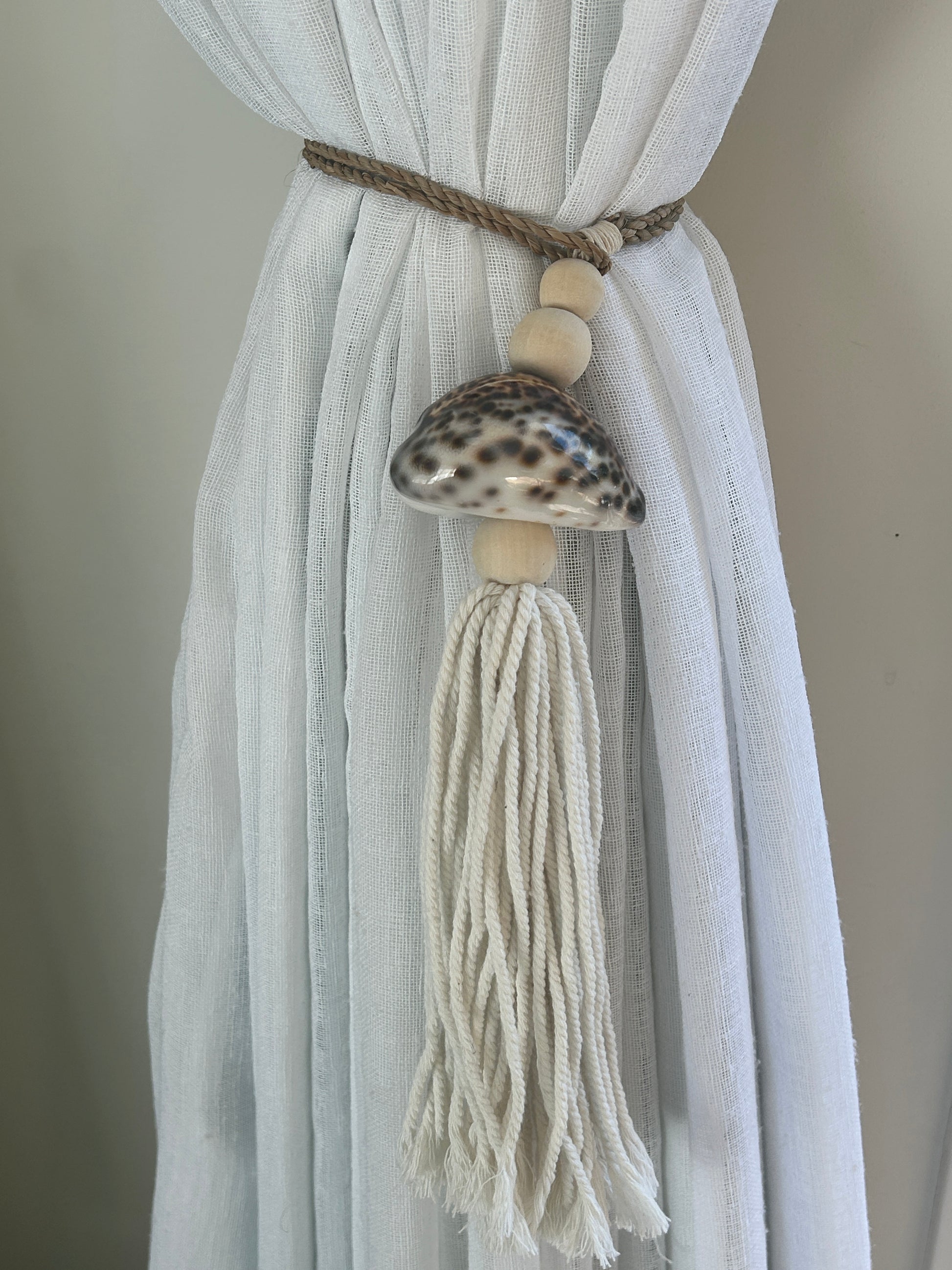 Decorative curtain tieback with shell and tassel on a white curtain against a neutral background