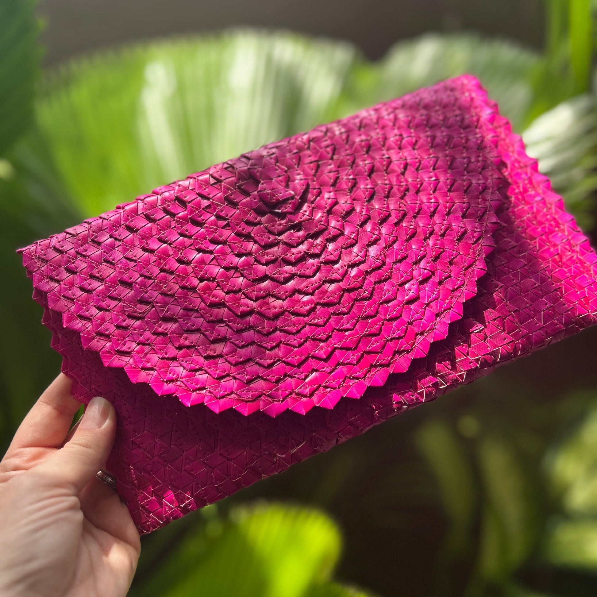 Pink textured clutch held by a hand with a green leafy background