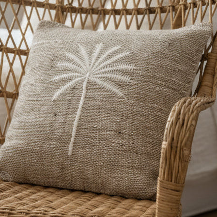 Textured mushroom coloured cushion with an embroidered white palm tree design on a wicker chair