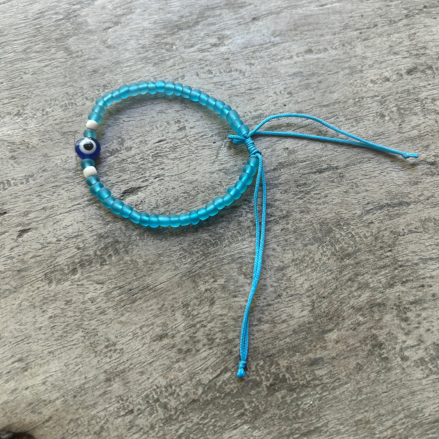 Blue beaded bracelet with an evil eye charm on a wooden surface