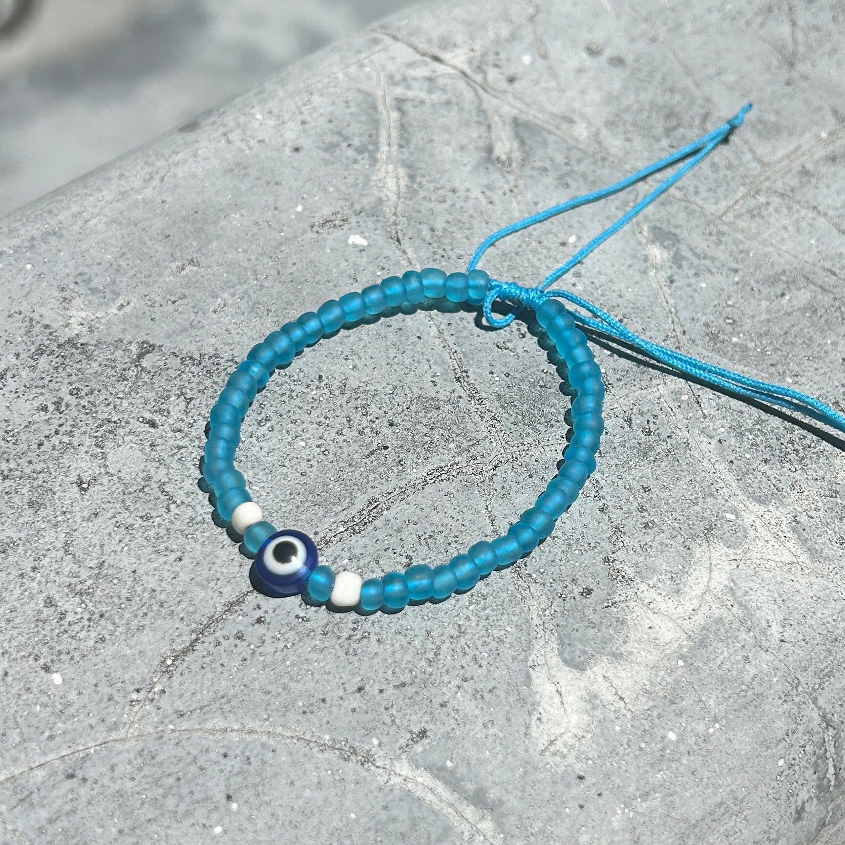 Blue beaded bracelet with an evil eye charm on a gray stone surface