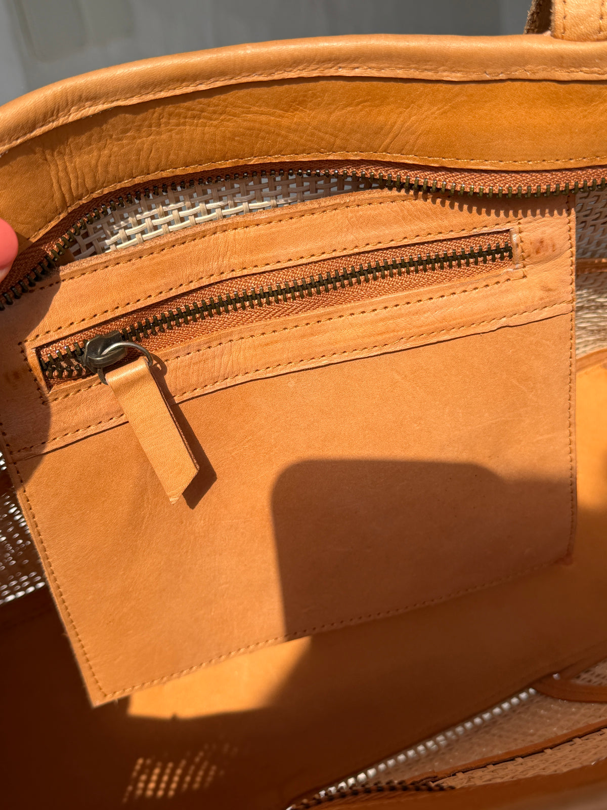 Close-up of a tan leather zippered pouch or organizer pocket inside a matching bag, with a small leather pull tab and dark metal zipper.