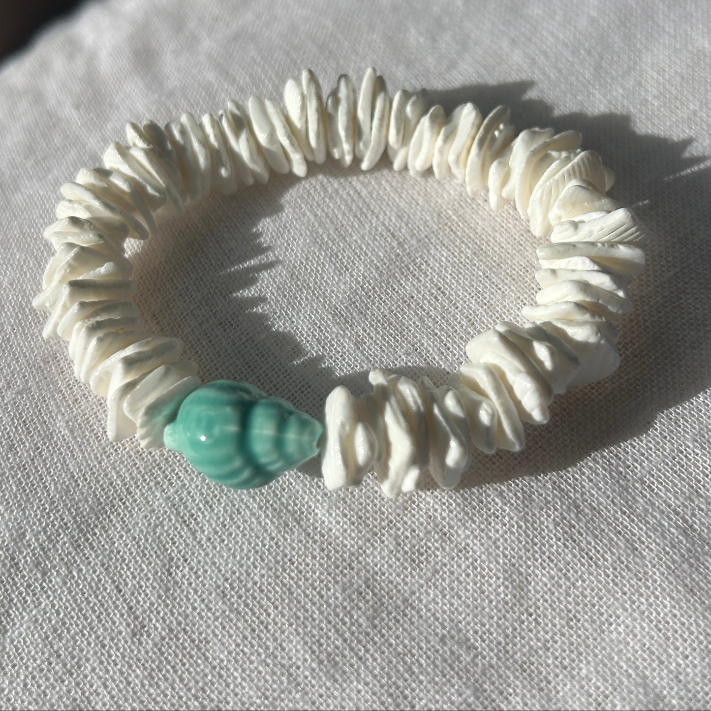 White shell bracelet with a turquoise bead on a light fabric background