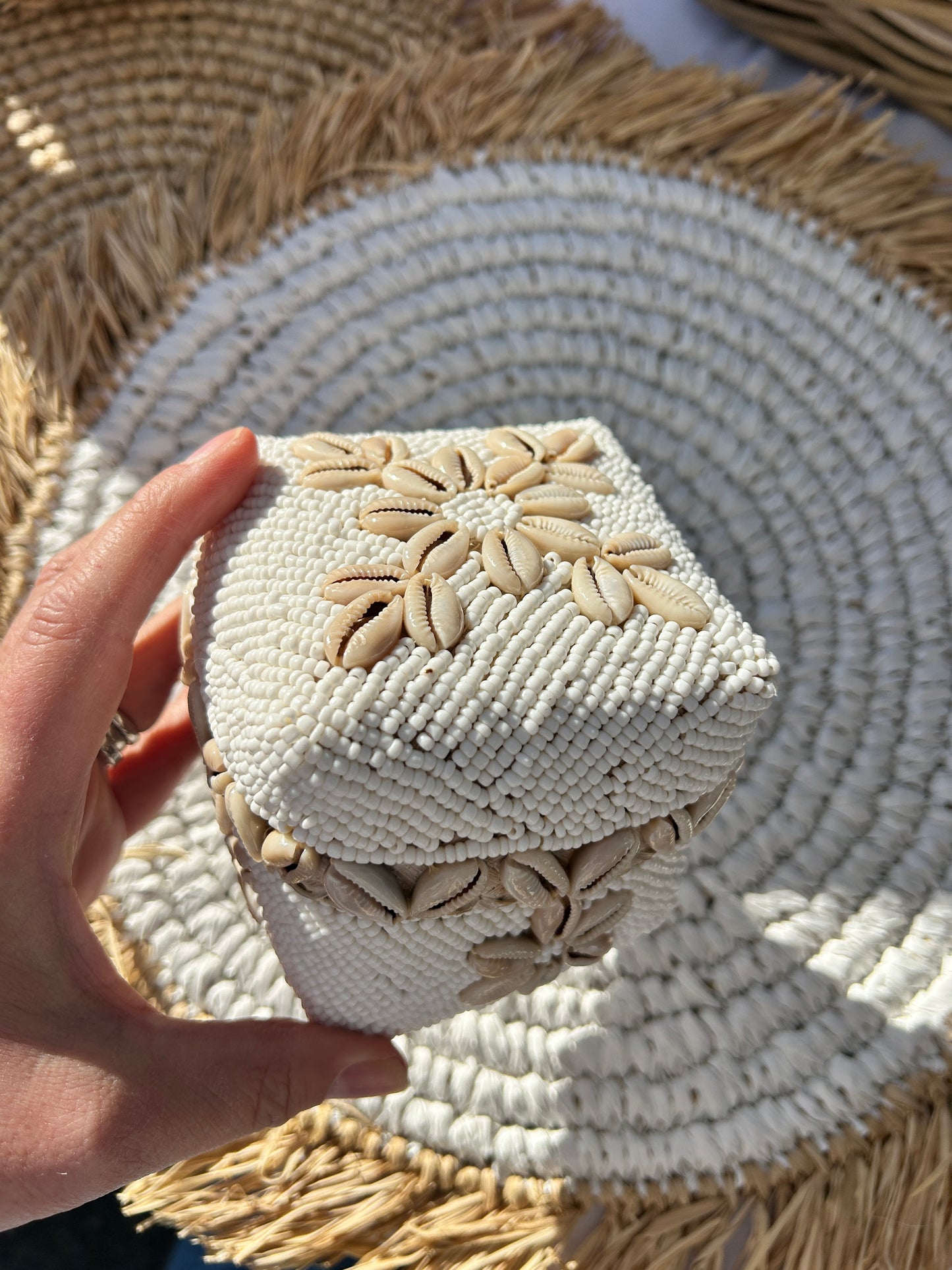 Hand holding a white hand beaded trinket box with natural coloured cowrie shell design