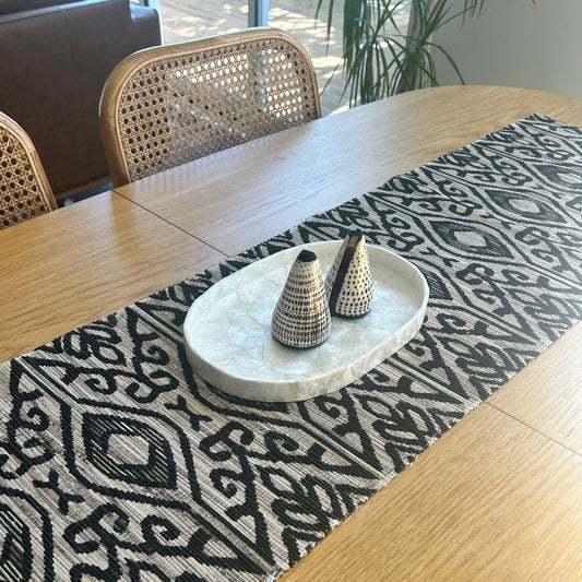 Decorative black and natural patterned ikat table runner on a capiz shell tray with shell salt and pepper shakers.