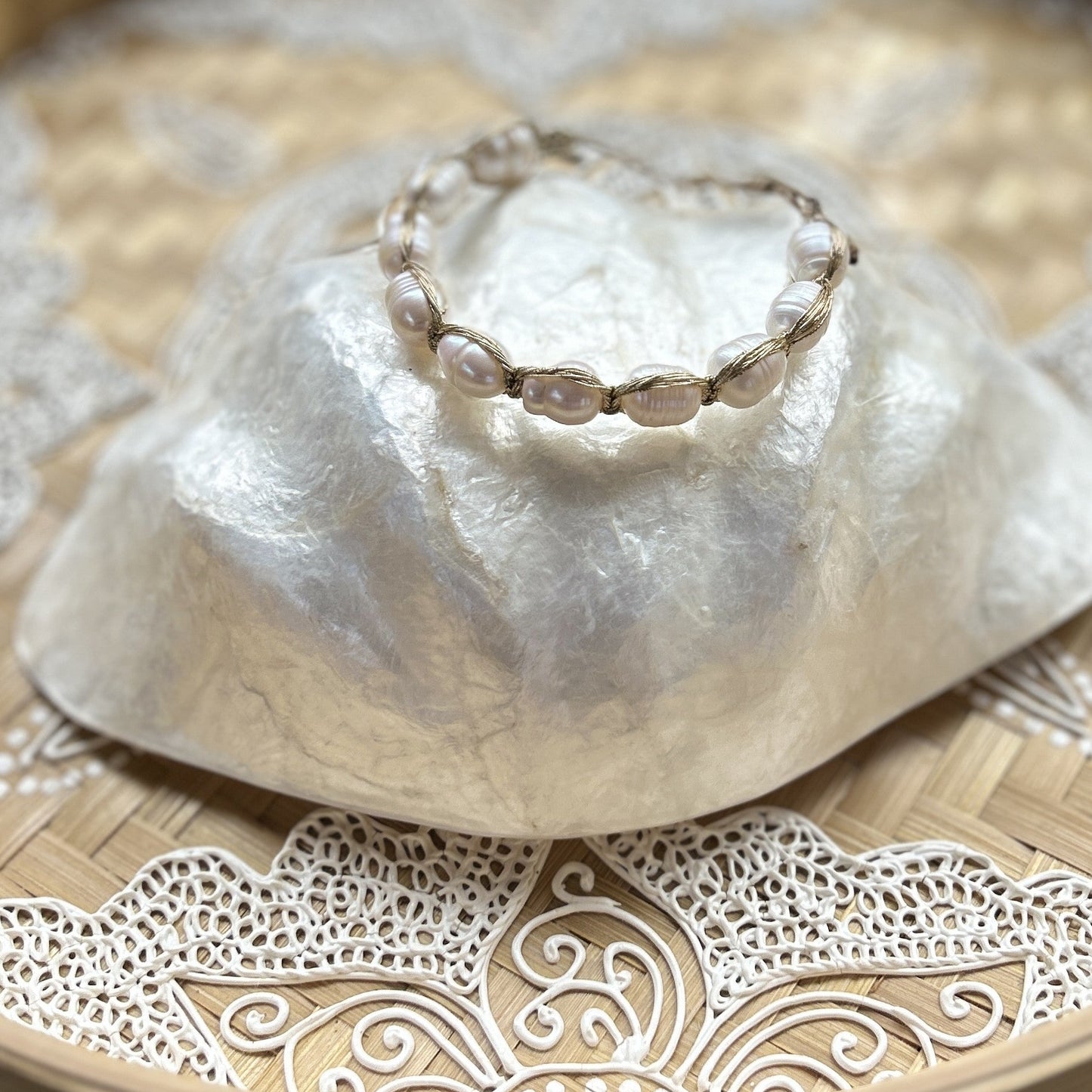 A bracelet with large pearls on gold string, displayed on a white surface with a patterned border.