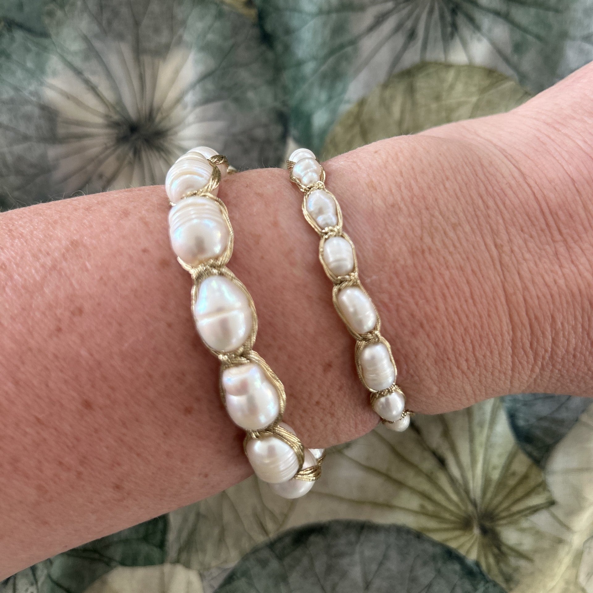 Two pearl bracelets on a wrist with a floral patterned background
