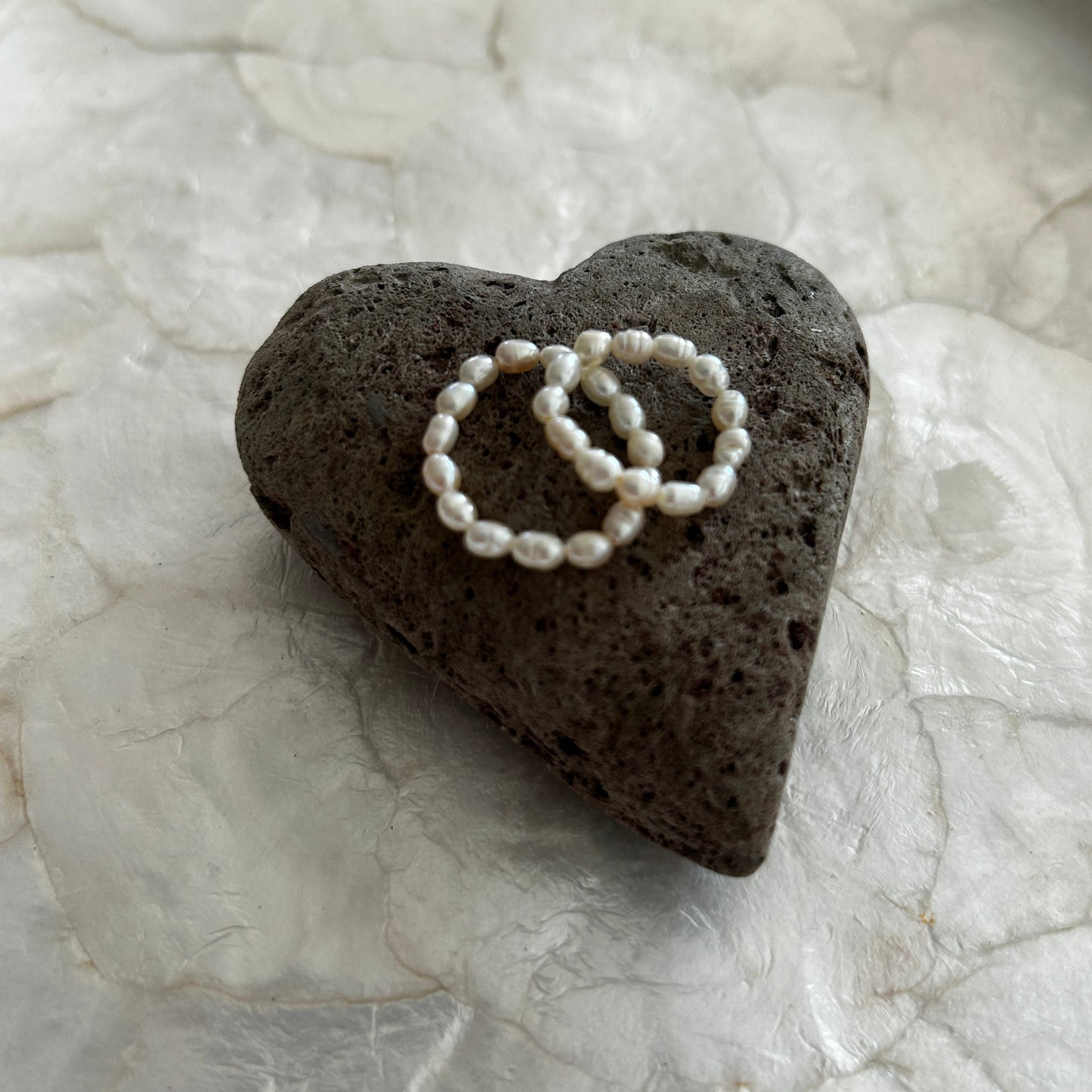 Heart-shaped black pummice stone with two mini freshwater pearl rings on a capiz shell tray 