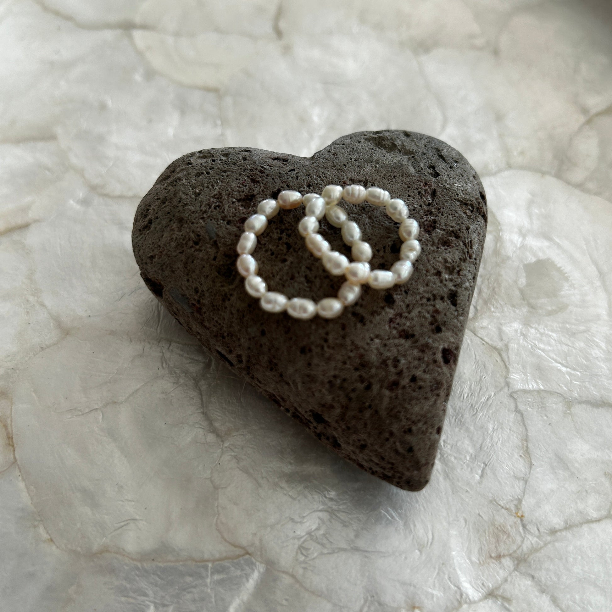 Heart-shaped black pummice stone with two mini freshwater pearl rings on a capiz shell tray 