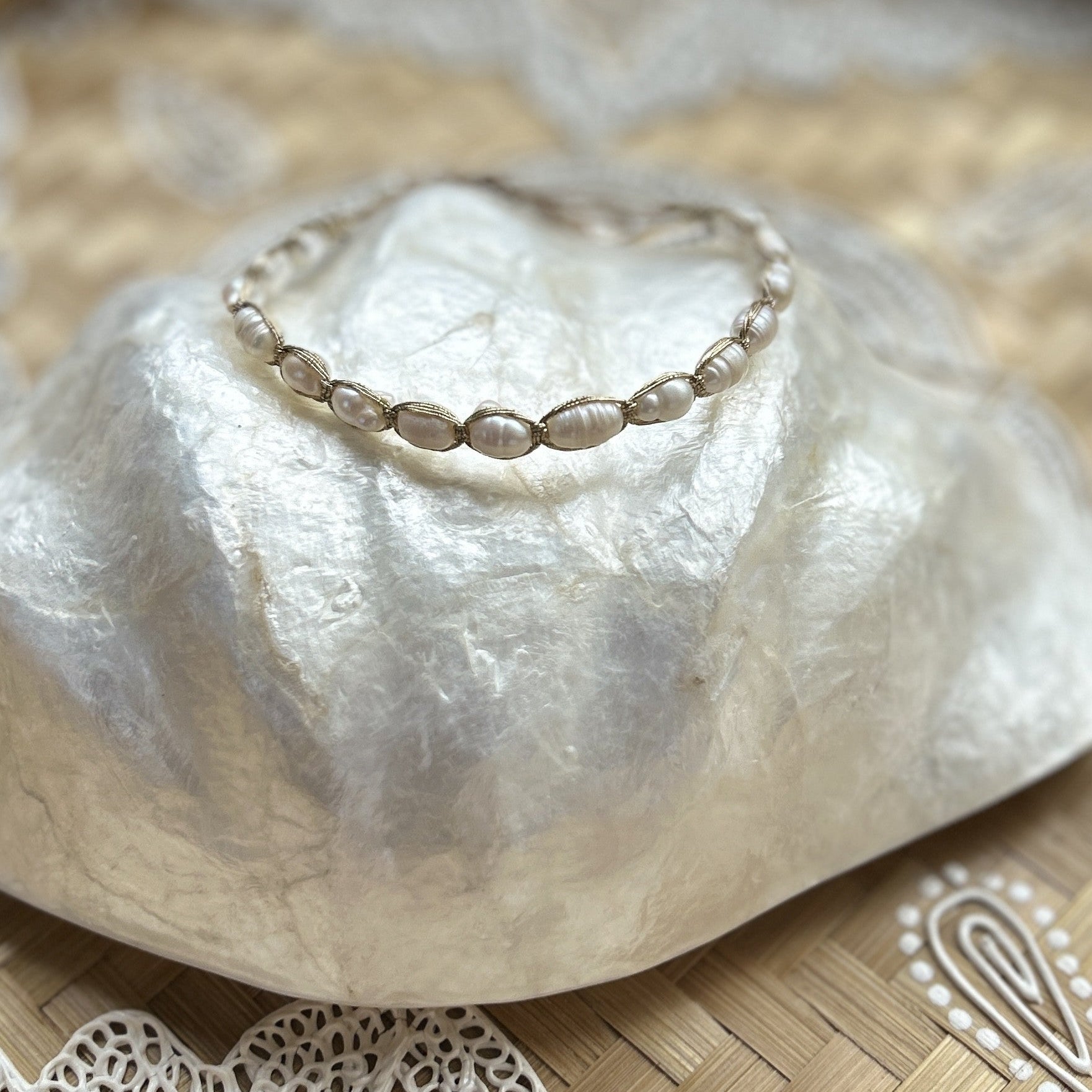 A bracelet with small pearls on gold string, displayed on a capiz shell bowl atop a woven basket