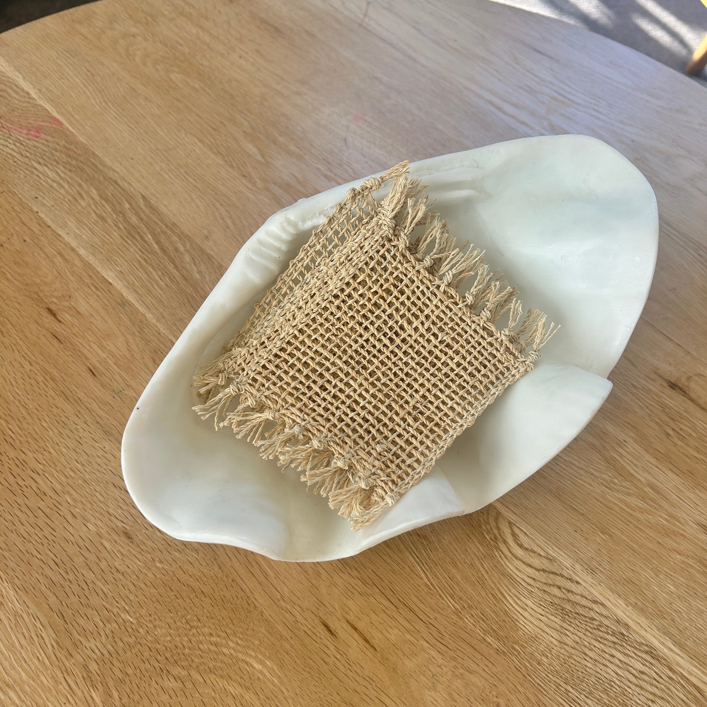 Woven rectangular jute coasters in a white dish on a wooden table - set of 4.