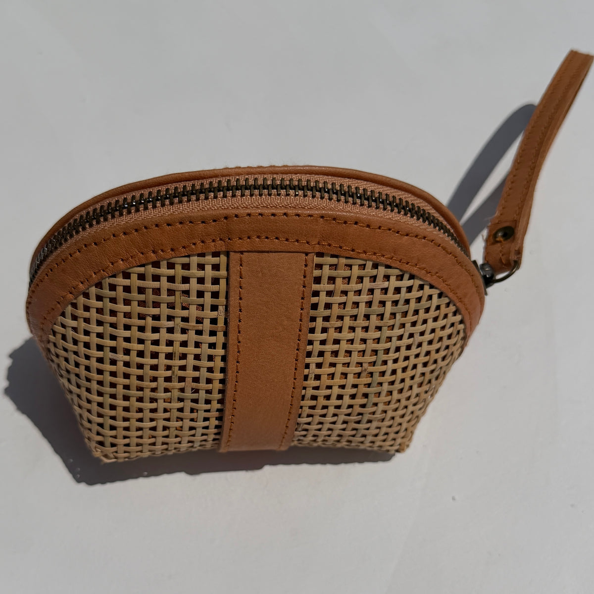 A small zippered pouch with a woven natural fiber body and tan genuine leather trim, shown on a plain light background.