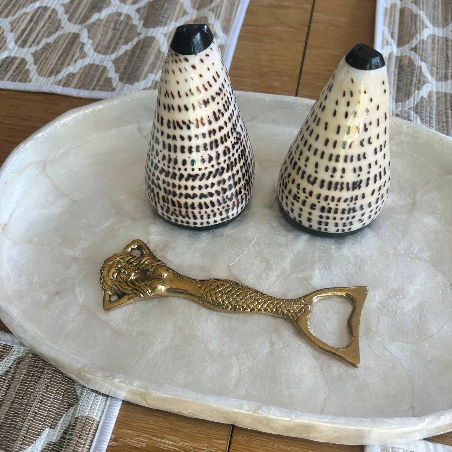 Conical shell salt and pepper shakers on a capiz shell tray with a mermaid brass bottle opener