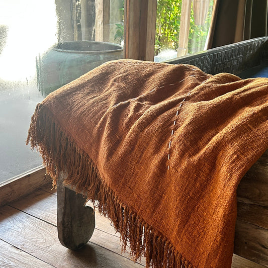 Terracotta blanket throw across wooden bench in a room with large windows.